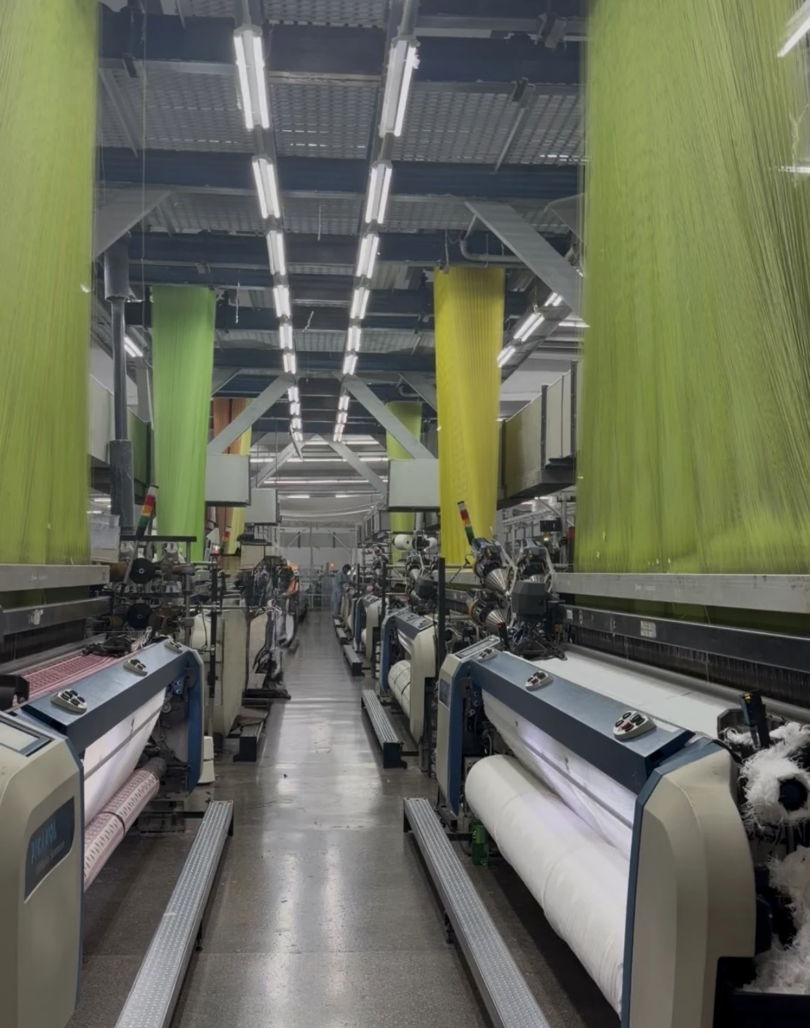 Original weaving floor in a selected textile manufacturing facility in Pakistan, showing active looms and coloured warp sheets